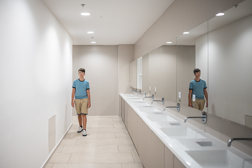 A teenager in front of the sinks in a minimalist sterile clean toilet with mirrors. Copy space.