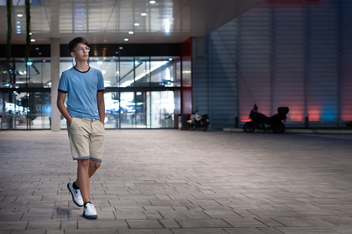 A teenager walking in the evening in front of the entrance to an illuminated building.