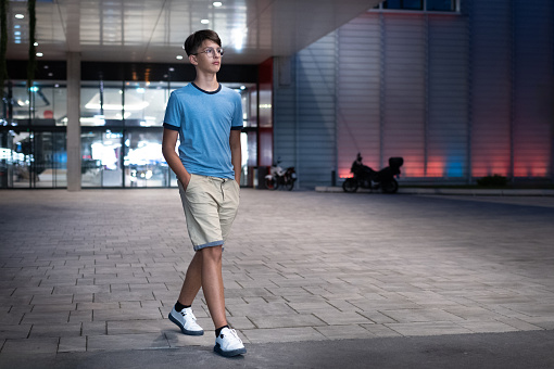 A teenager walking in the evening in front of the entrance to an illuminated building.