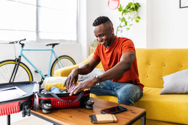 istock Young african man packing clothes to luggage before going on summer holidays 1899995567