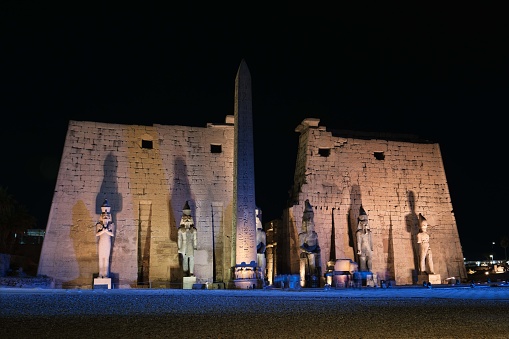 Luxor, Egypt - December 26 2023: Luxor Temple main entrance, first pylon with obelisk and statues of Ramesses II at night