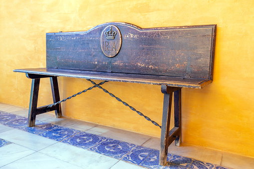 Seville, Spain - December 22, 2023: Wooden bench in the Alcazar of Seville, Spain. The Alcazar, which dates back to the 12th century, forms part of a UNESCO World Heritage site.