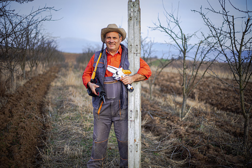 Portrait of a farmer with equipment for pruning branches in an orchard