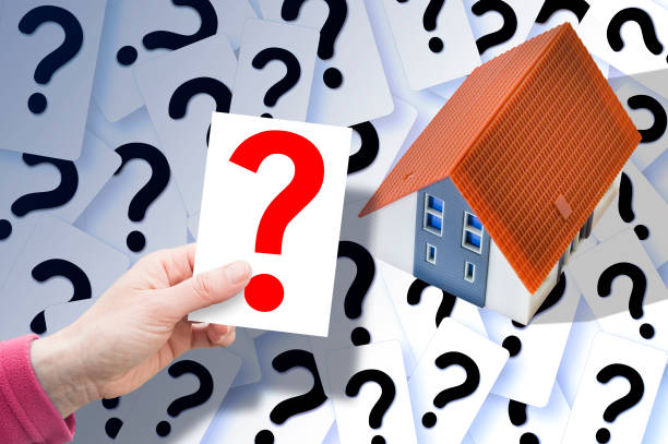 istock Doubts and questions about buildings - concept with home model against question marks and hand with ticket 1900055587