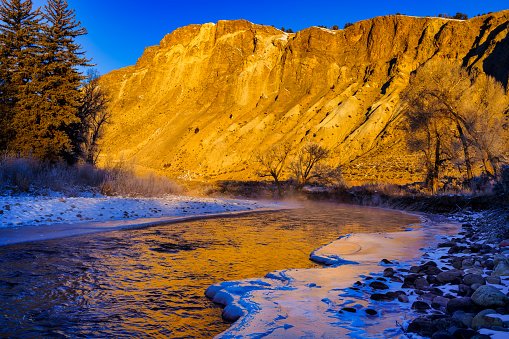 Golden Sunrise Light Cold River Landscape - Scenic views along mountain river in winter with golden light contrasting with cool blue shadows. Ice and icy reflections in water.