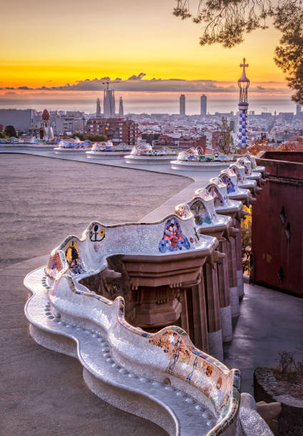 Morning at Parc Guell with Antoni Gaudi mosaic bench in Barcelona with city skyline and a orange sky with clouds minutes before the sun rises