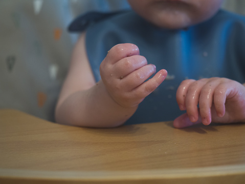 Close up shot of hands of unrecognizable baby sitting in high chair ready to eat