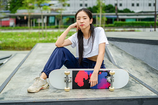Portrait of female skateboarder sitting on the gound of skateboarding park in city