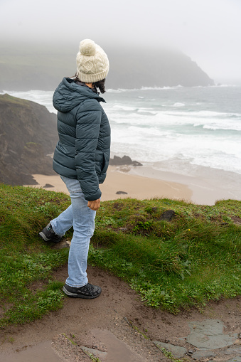 Woman from behind looking out at a beautiful view of the Irish coast a foggy and rainy day