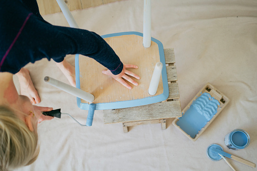 Transformation in progress: Woman channels creativity onto an antique chair with blue hues.