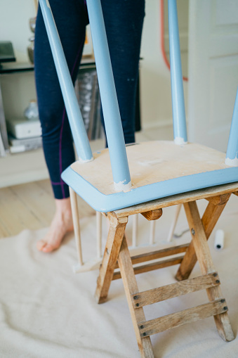 Artful renewal: Woman's passion for DIY reflects in the meticulous blue painting of an old chair.