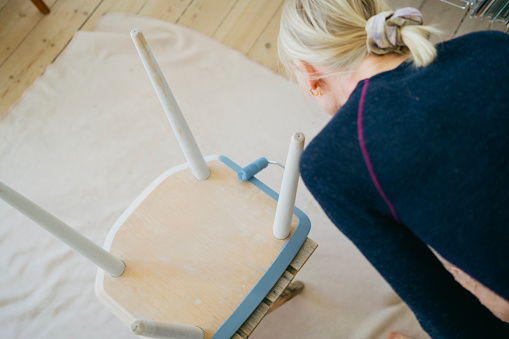 Creative restoration: Woman's DIY journey unfolds with blue paint on an old chair.