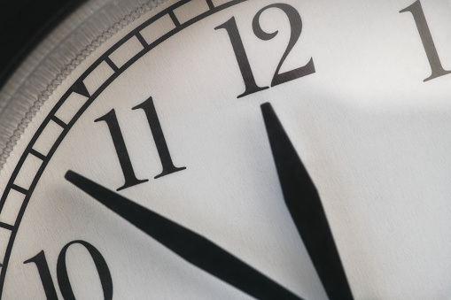 A clock with the hour hand pointing at twelve and the minute hand between 10 and 11. Close up.