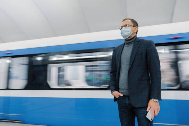 istock Commuter in blue suit and mask stands in subway station, blurred train in motion behind, depicting urban life during the pandemic 1900215810