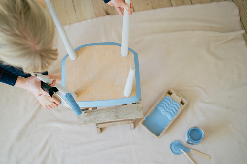 DIY charm: Woman's hands bring character to an old chair with a blue paint palette.