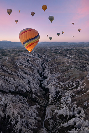 a group of hot air balloons over the rocky landscape of cappadocia at sunrise, the balloon in the foreground is illuminated by the flames of the burner, fairy chimneys in turkey, vertical