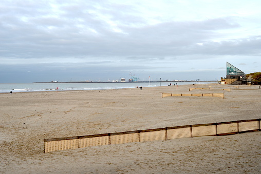 Blankenberge, West-Flanders, Belgium - December 30, 2023: view from beach promenade on the O Neill surf club house and walking tourists. Sea-Bruges port on the horizon on a sunny day