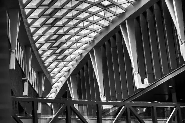 Black and white image of a modern building interior with a geometric glass ceiling and angular beams.