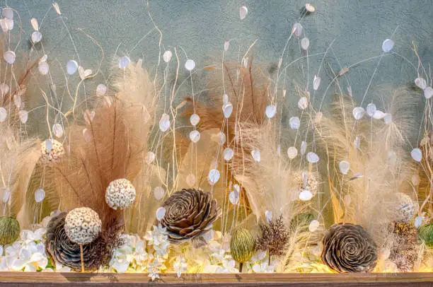 Dried floral arrangement with pampas grass, seed heads, and decorative spheres against a textured background.