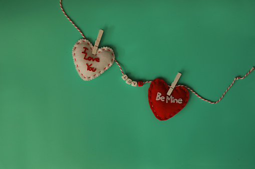 Two heart shapes with the words I love you and hugs and kisses hanging on a string with clothespin.   The word Love in between spelled out in beads on the string On a sea foam green background.