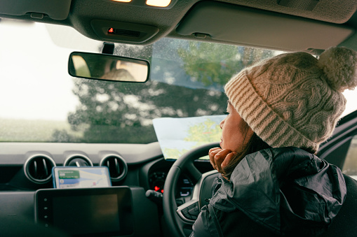 Woman with knit hat inside her car seen from behind while checking her cell phone and map to find out her route