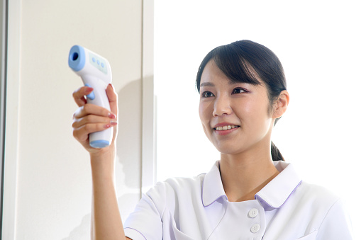 A young Asian female medical worker measuring body temperature with a radiation thermometer