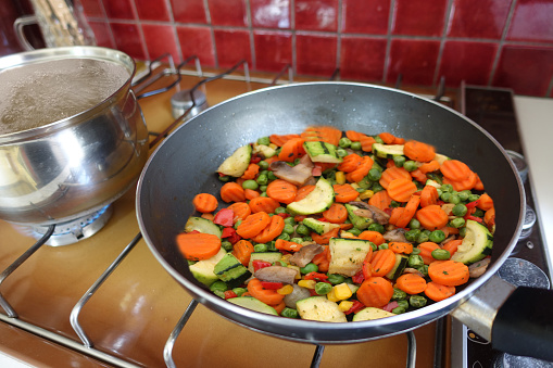 Portioned mixed vegetables being cooked and a pot of boiling water on a gas hob
