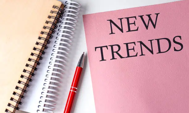 Photo of NEW TRENDS word on the pink paper with office tools on white background