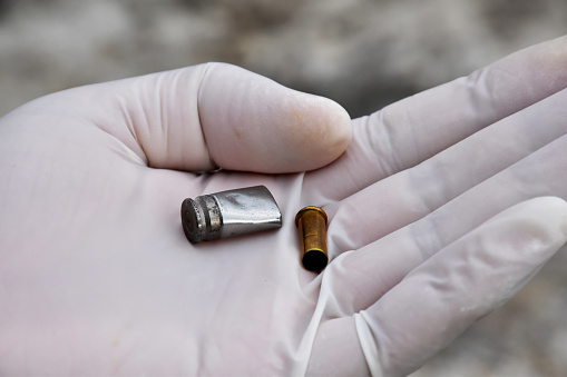 Forensic officers holds physical evidence which is the bullet shell up to eye level to determine the size and type of ammunition at the murder. Soft and selective focus.