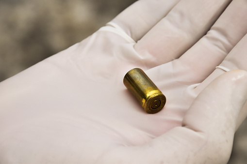 Forensic officers holds physical evidence which is the bullet shell up to eye level to determine the size and type of ammunition at the murder. Soft and selective focus.
