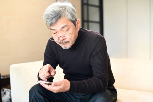 An elderly Asian man with white hair operating a smartphone