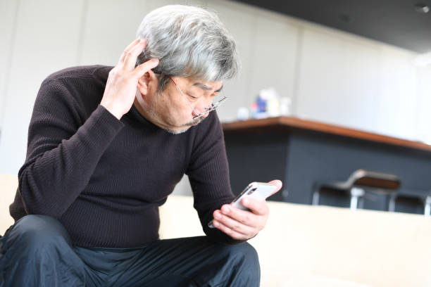 istock An elderly Asian man with white hair is operating a smartphone with a troubled expression on his face. 1900732414