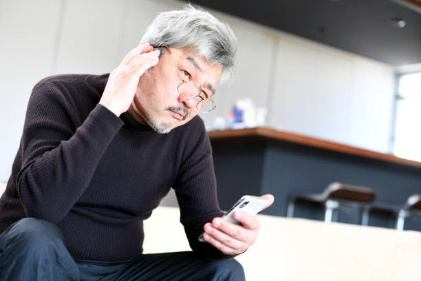 istock An elderly Asian man with white hair is operating a smartphone with a troubled expression on his face. 1900732420