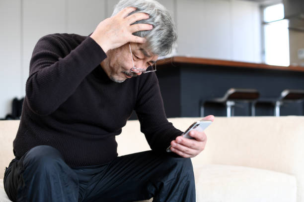 istock An elderly Asian man with white hair is operating a smartphone with a troubled expression on his face. 1900732932