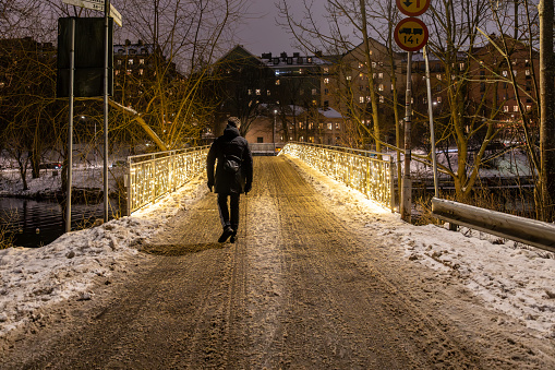 Stockholm, Sweden Dec 12, 2023 A man walks over a small illuminated bridge at Chrstmas time over the Palsundet canal.
