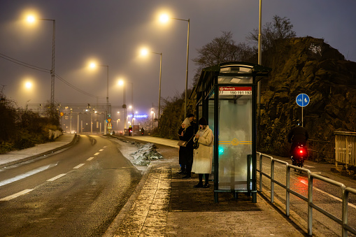 Stockholm, Sweden Dec 20, 2023 Pedestrians in the Liljeholmen district waiting for a bus in the early morning fog.