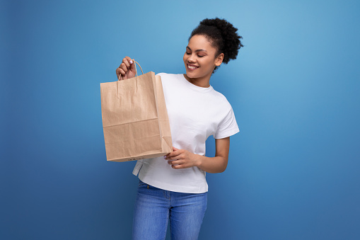 young pretty hispanic business music lover woman in white t-shirt holding craft package for store delivery.