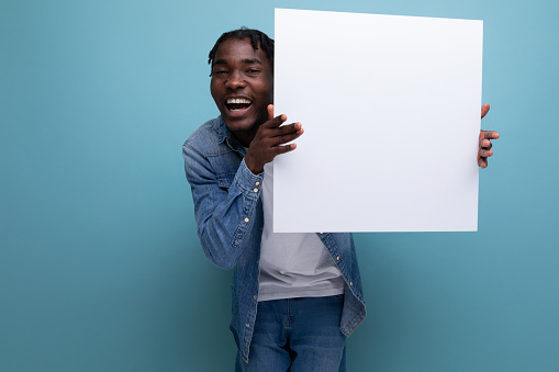 American man with dreadlocks in a denim jacket demonstrates a paper poster with a mockup.