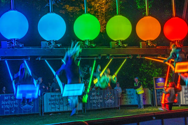 Children playing on illuminated swings at the Festival of Lights in New Plymouth. There is some motion blur due to the long exposure. People at the far side are not blurred. The scene is brightly lit by the coloured swings.