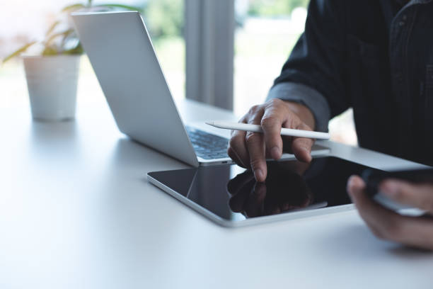 istock Business man using digital tablet and working on laptop computer with mobile phone on table at home office. Working at home, telecommuting, e-learning 1900839969