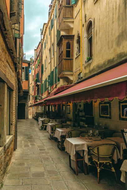 Table set with a pink rose centerpiece, cutlery, and wine glasses, overlooking a narrow canal in Venice, Italy