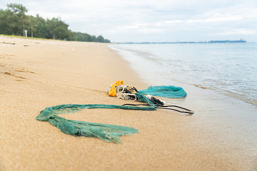 Abandoned plastic fishing net left by human activity on a beautiful beach at the famous sightseeing place. Human waste disposal impacting the environmental issue of the coast and sea ecosystem.