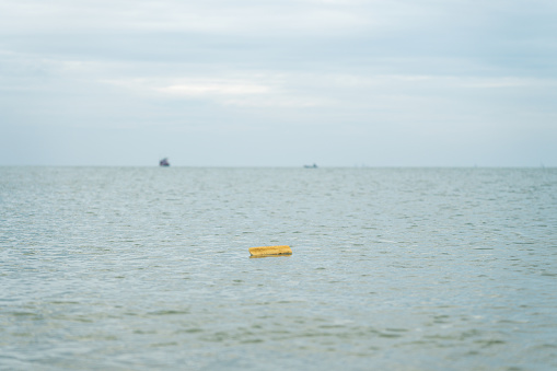 Scenic view of the sea with a single yellow plastic foam floating on a sea surface contaminated the sea and ecosystem of sea life. Environmental contamination caused by human activity requiring the environmental cleanup.