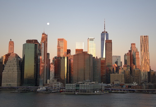 New York, NY.  Dec. 9, 2022. \n Sunrise reflecting on the east side of Manhattan Island while morning moon is still visible in the sky.