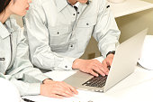 An Asian male office worker and a female employee wearing work clothes are having a conversation while operating a laptop.