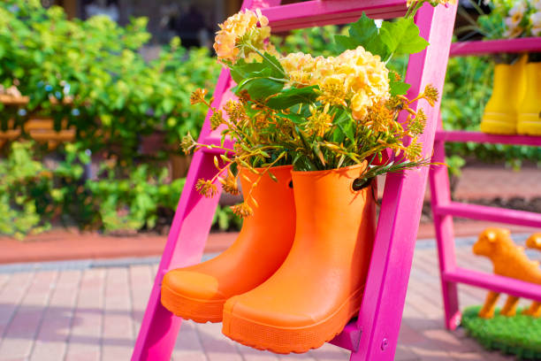 flowering plant in orange rubber boots, on a pink stepladder, stairs on a sunny spring or summer day, outside.