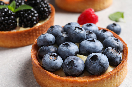 Tartlets with different fresh berries on light table, closeup. Delicious dessert