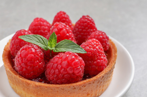 Tartlet with fresh raspberries and mint on light table, closeup. Delicious dessert