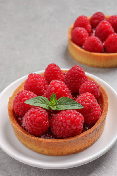 istock Tartlets with fresh raspberries and mint on light grey table. Delicious dessert 1900996591