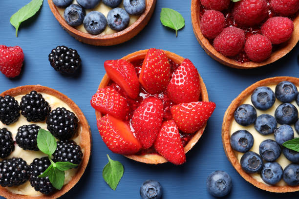 istock Tartlets with different fresh berries on blue wooden table, flat lay. Delicious dessert 1900997093